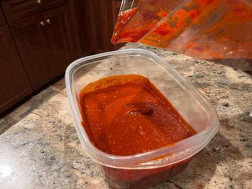 Pouring red chile sauce into a storage container.