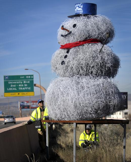 A crew from AMAFCA, including James Moya, left, and John Nix, right, do the finishing touches on the 12-foot high tumbleweed snowman westbound on Interstate 40, east of University Blvd., in 2013. This was the 18th year for the snowman, who had recently been photographed and published in National Geographic magazine. (Albuquerque Journal file photo by Marla Brose)